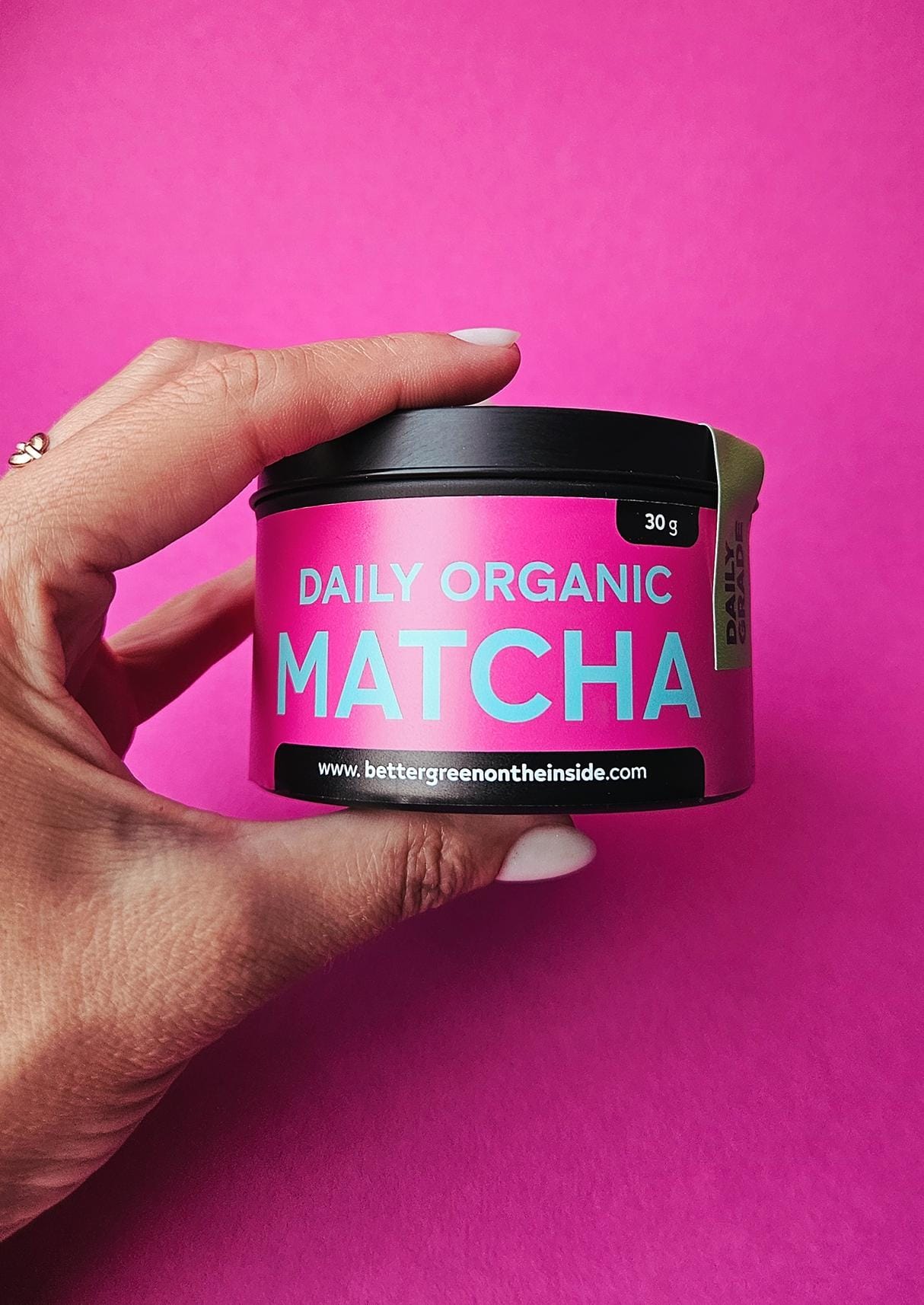 Hand holding a pink container of 'Daily Organic Matcha' against a pink background